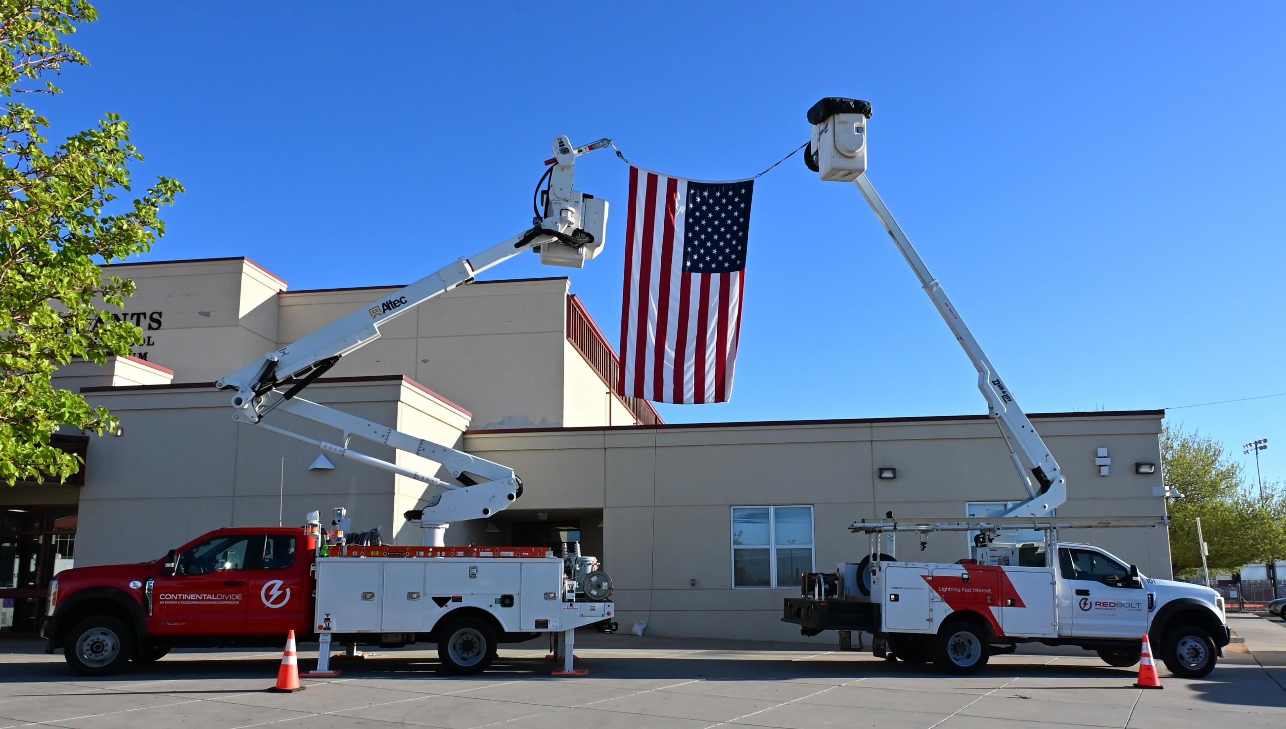 Two bucket trucks with extended arms holding the american flag between them